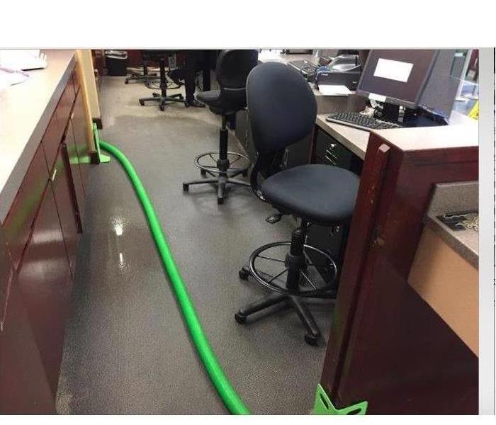 Green hose that crosses through an office floor, wet carpet, office chair, desk, computer