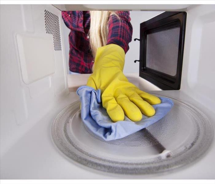 hand with yellow plastic glove cleaning the inside of a microwave